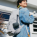 Image of a woman outside a white building wearing a backpack with a black SRS-XB100 attached via its strap