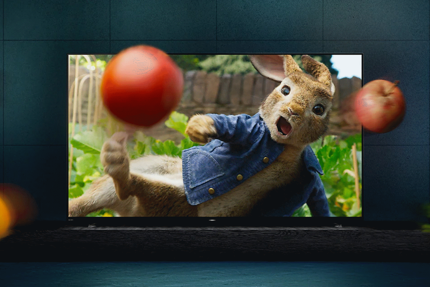 TV BRAVIA en una base con la película Peter Rabbit en pantalla con frutas y vegetales saliendo de la TV.
