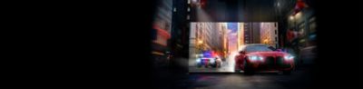 Красный автомобиль и преследующий его полицейский автомобиль выезжают из экрана телевизора BRAVIA на улицу города
