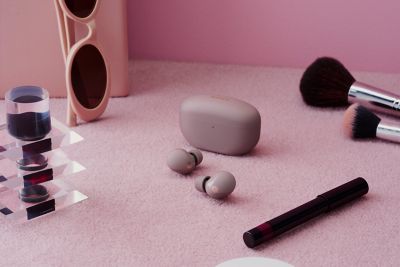 The new WF-1000XM5 Noise Cancelling sat on a makeup table along with a pair of sunglasses and other makeup accessories