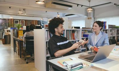 Two colleagues in a meeting in an open-plan office, one of whom is wearing LinkBuds Open earbuds.