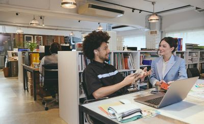 Two colleagues in a meeting in an open-plan office, one of whom is wearing LinkBuds Open earbuds.