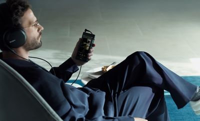 Man sittande i en fåtölj med Sony NW-WM1AM3 i handen och hörlurar på