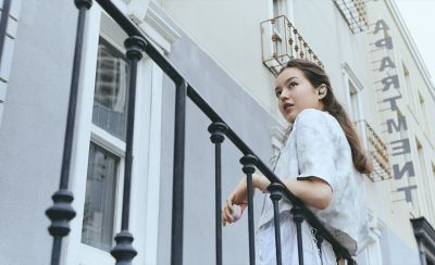 A young woman wearing a pair of LinkBuds Open earbuds leaning on a railing.