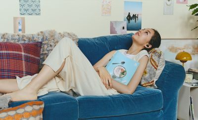 A young woman wearing a pair of LinkBuds Open reclining on a sofa.