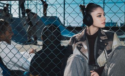 A young person sitting in a busy skate park wearing the ULT WEAR headphones.