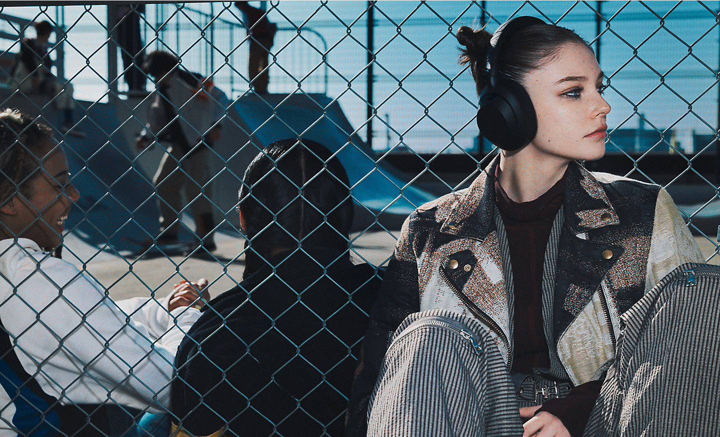Một thanh niên đeo tai nghe ULT WEAR, ngồi tại sân trượt ván đông đúc.
