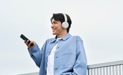 Usmívající se muž v bílých sluchátkách WH-CH530 držící venku smartphone