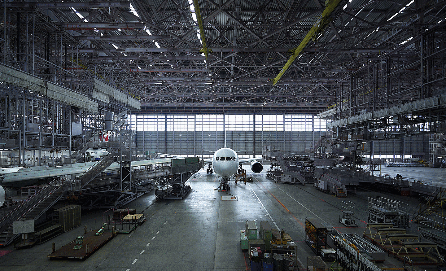Interior of a large aircraft hangar with a passenger aircraft parked inside and equipment on the floor.