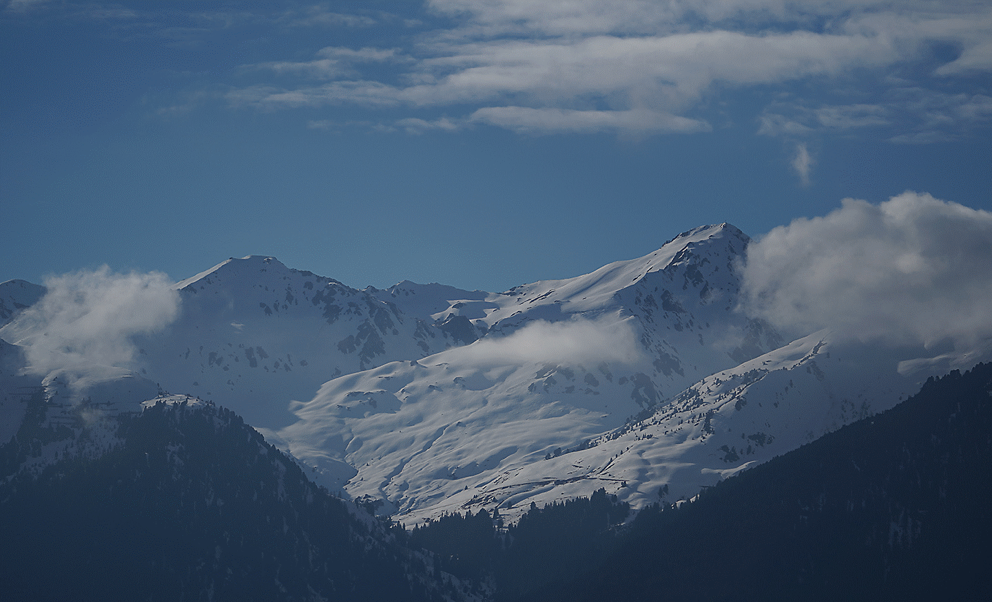 Snow-covered mountain peaks appearing visually compressed and close together under a blue sky with scattered clouds.