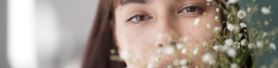 Close-up portrait of a woman with soft background blur and small white flowers in the foreground.