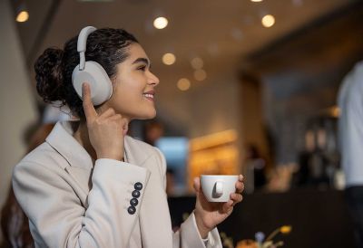 Image of a person wearing a pair of Sony headphones and tapping the earcup with one finger, on a blurred background