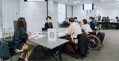 Employees and wheelchair user are sitting around a table and discussing