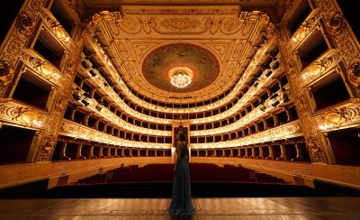 Symmetrical interior view of an ornate opera house with golden balconies and a person standing on the stage.