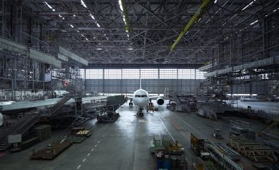 Interior of a large aircraft hangar with a passenger aircraft parked inside and equipment on the floor.