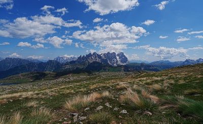 Wide landscape view of mountains under a blue sky with scattered clouds and grassy terrain in the foreground.