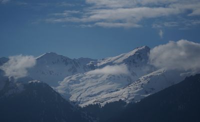 Snow-covered mountain peaks appearing visually compressed and close together under a blue sky with scattered clouds.