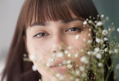 Close-up portrait of a woman with soft background blur and small white flowers in the foreground.