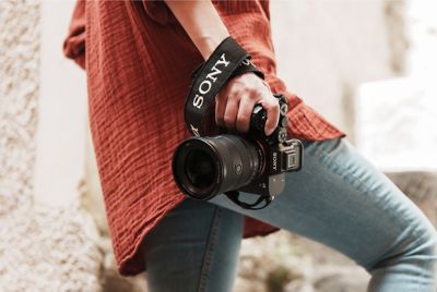 Prim-plan cu o persoană ținând camera în mâna dreaptă, în timp ce urcă scări relaxat, cu obiectivul FE 16–35 mm F2.8 GM montat