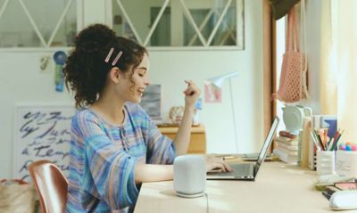 A young woman working at a laptop on a desk with the LinkBuds Speaker in the foreground.