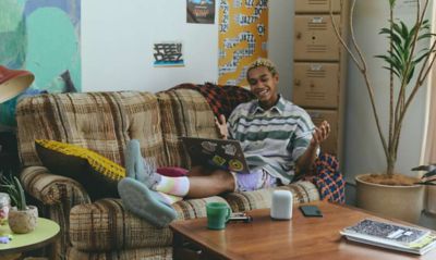 A young man sat on a sofa with a LinkBuds Speaker on a coffee table in the foreground.