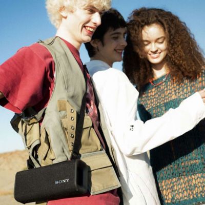 Dos mujeres y un hombre con un ULT FIELD 3 en su hombro disfrutan del baile.