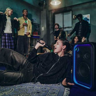 Personas disfrutando de la música en una fiesta en un espacio interior mientras una mujer canta karaoke con los ULT TOWER 5 y ULTMIC1.